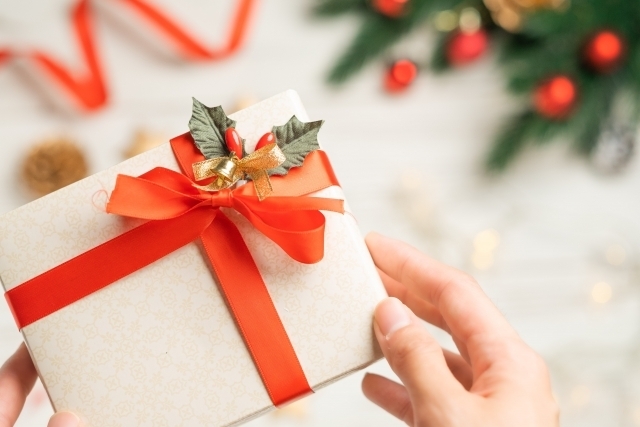 赤いリボンのついたクリスマスプレゼントの包みを持つ手